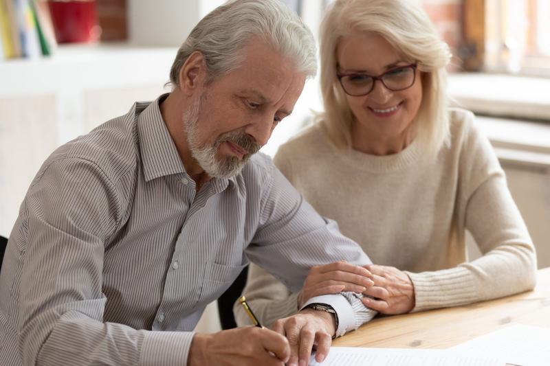 Happy older family couple husband and wife sign legal paper insurance contract write will 